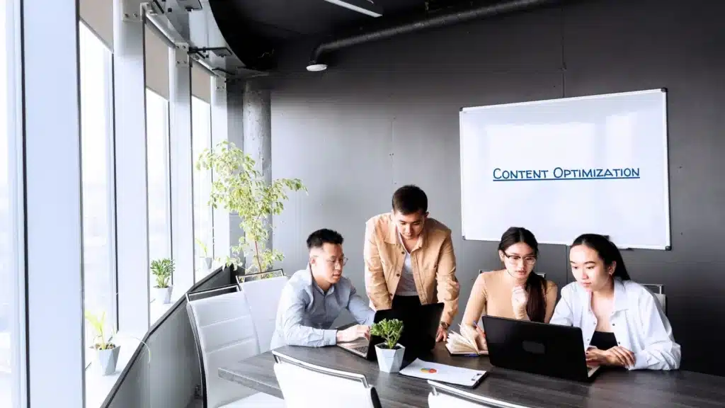 Team working on SEO content optimization strategies using laptops in a bright, modern office with a whiteboard labeled “Content Optimization.